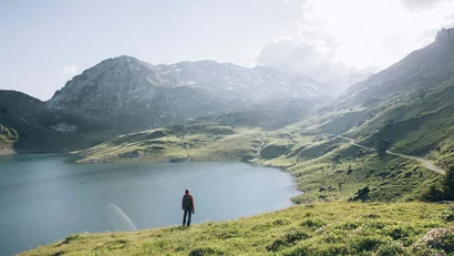 Person steht an einem See in den Bergen bei Sonnenlicht