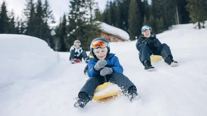 Kind mit Skibrille fährt auf einem Schlitten durch den Schnee