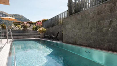 Moderner Außenpool mit Liegestühlen und Bergblick bei Sonnenschein