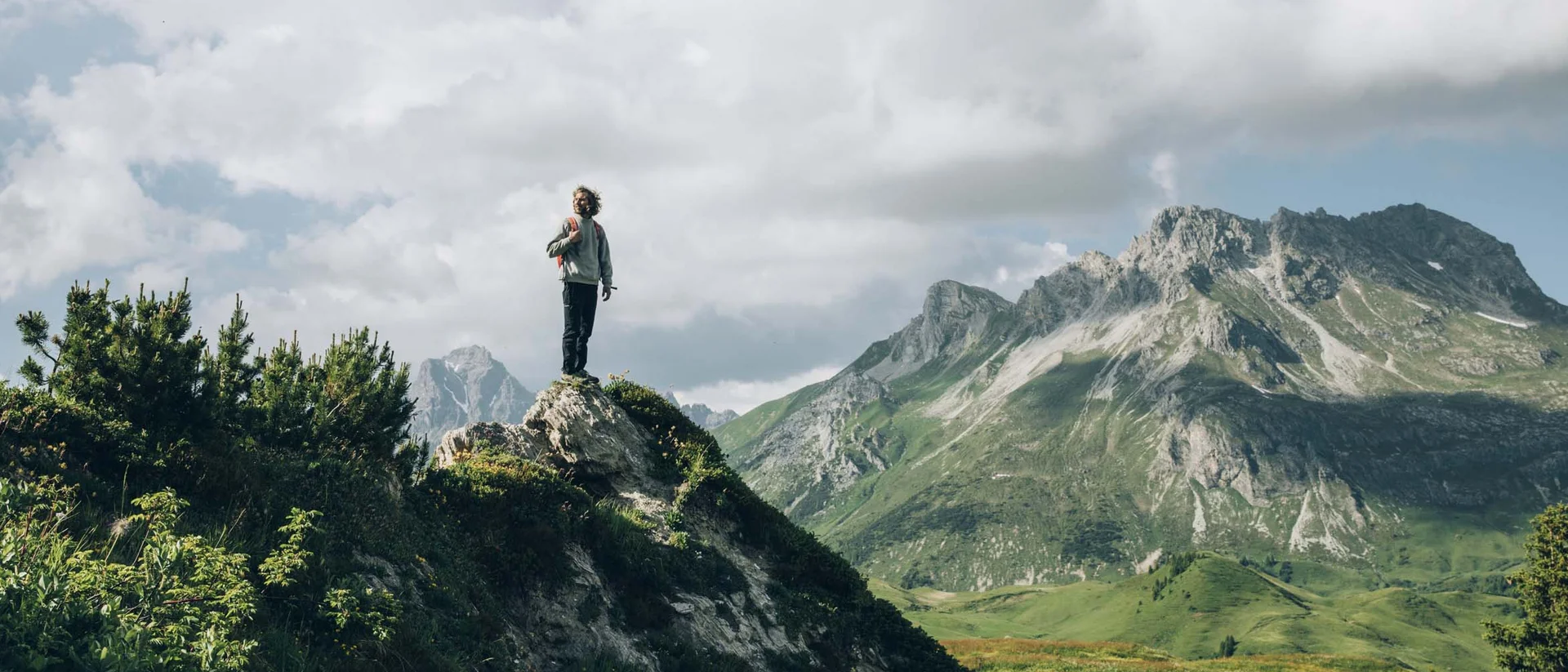 Hohe Welt – 4 Luxury Apartments in Oberlech Mann steht auf Berggipfel mit Blick auf bewachsene Berge und bewölkten Himmel