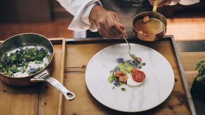 Koch richtet kunstvoll ein Gericht mit Garnelen, Tomate und Kräutern an