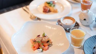 Fein angerichteter Lachs mit Brotchips, Kaffee und Orangensaft auf weißem Tisch