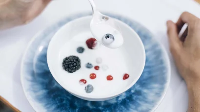 Löffel mit Joghurt und Beere über Schüssel mit Beeren und Joghurt