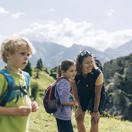 Frau und zwei Kinder wandern in den Bergen mit Rucksäcken bei Sonnenschein