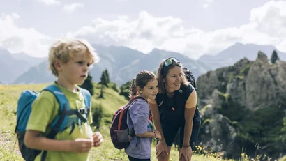 Frau und zwei Kinder wandern in den Bergen mit Rucksäcken bei Sonnenschein