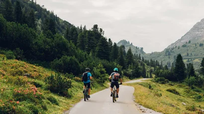 Zwei Radfahrer fahren auf Bergstraße durch bewaldete Landschaft