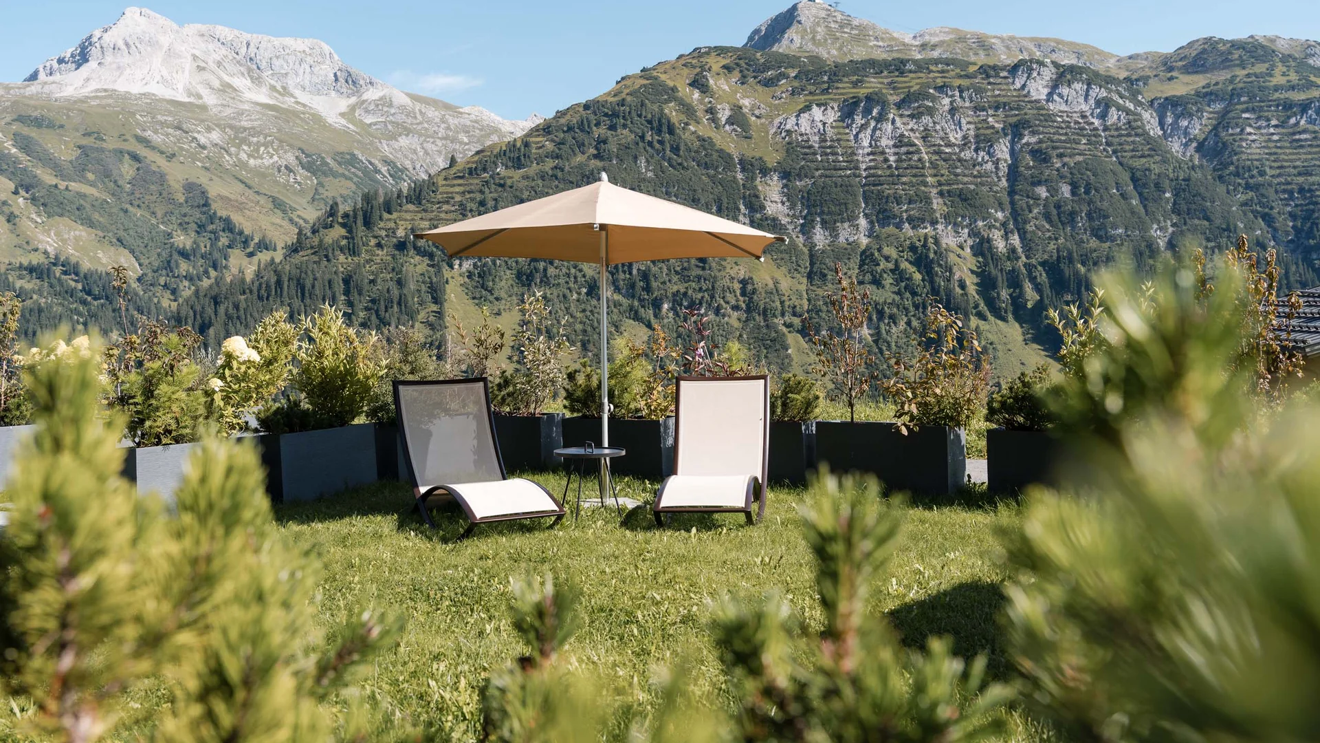 Zwei Liegestühle mit Sonnenschirm in Garten mit Bergblick
