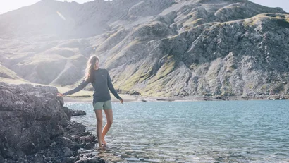 Frau steht am Ufer eines klaren Bergsees mit Bergen im Hintergrund