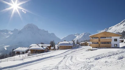 Verschneites Bergdorf mit Chalets und schneebedeckten Gipfeln bei strahlendem Sonnenschein