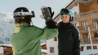 Zwei Skifahrer mit Helmen geben sich einen Highfive im verschneiten Dorf