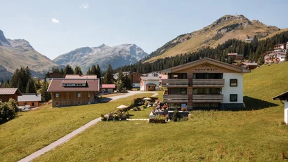 Alpenlandschaft mit Häusern, grünen Wiesen und Bergen im Hintergrund