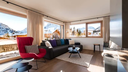 Helles Wohnzimmer mit Sofa, rotem Sessel und Bergblick durch große Fenster
