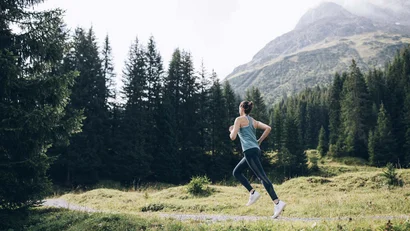 Frau joggt auf einem Waldweg in den Bergen bei bewölktem Himmel