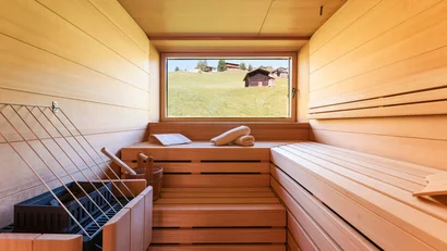 Innensauna mit Holzbank und Fenster mit Blick auf grüne Hügel und Hütten