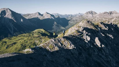 Zwei Wanderer auf einem Berggrat mit Bergmassiv im Hintergrund