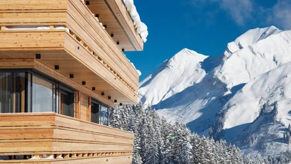 Holzgebäude mit verschneiten Balkonen vor schneebedeckten Bergen