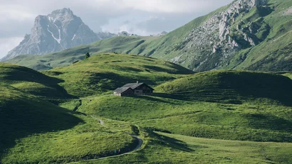 Grüne Hügel mit Wanderweg und Berghütte vor markantem Berggipfel