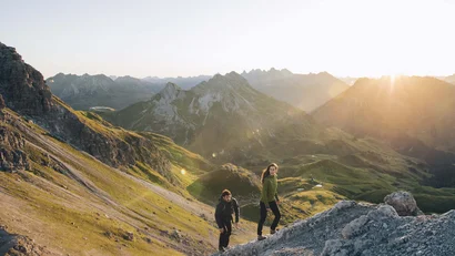 Zwei Wanderer steigen im Sonnenuntergang auf einen Berg in den Alpen