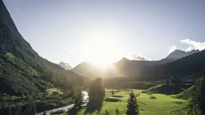 Sonnenaufgang über grüner Berglandschaft mit Fluss und Bäumen