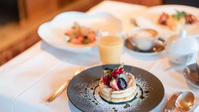 Pfannkuchen mit Beeren und Puderzucker auf einem schwarzen Teller