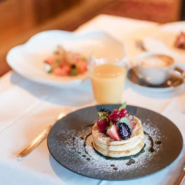 Pfannkuchen mit Beeren und Puderzucker auf einem schwarzen Teller