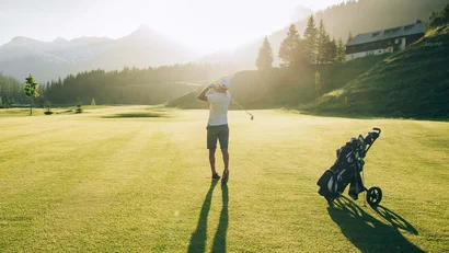 Golfer schlägt Ball auf sonnigem Berggolfplatz mit Golfwagen