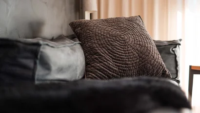 Braunes Kissen mit Muster auf grauem Sofa vor Vorhängen