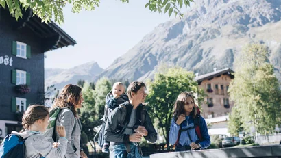 Familie wandert in den Bergen vor einem Dorf bei sonnigem Wetter