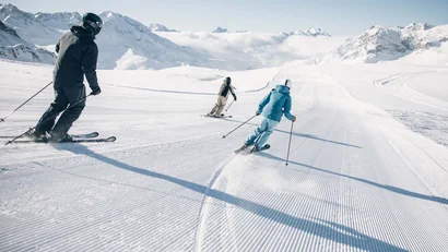 Drei Skifahrer fahren auf präparierter Skipiste in den Bergen