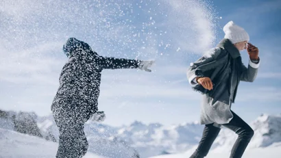 Zwei Menschen im Schnee vor verschneiten Bergen, einer wirft Schnee auf den anderen