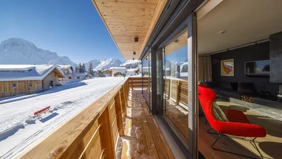 Holzbalkon mit Blick auf ein verschneites Bergdorf und die umliegenden Alpen