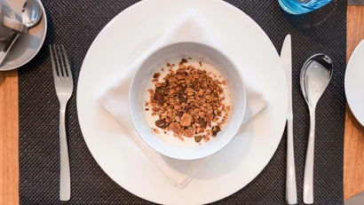 Schüssel mit Müsli und Joghurt auf weißem Teller am gedeckten Tisch