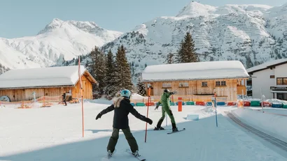Zwei Personen lernen Skifahren vor schneebedeckten Berghütten im Skiresort