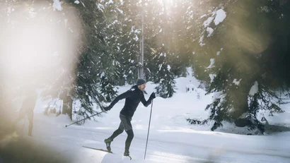 Mann beim Langlaufen durch verschneiten Wald bei Sonnenlicht