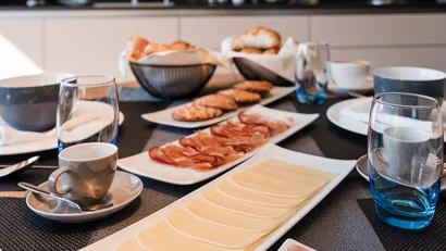 Frühstückstisch mit Aufschnitt, Käse, Brötchen und Kaffee in einer modernen Küche