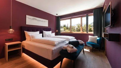 Modernes Schlafzimmer mit lila Wänden, gemütlichem Bett und Bergblick