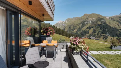 Balkon mit Tischen, Stühlen und Alpenblick bei klarem Himmel