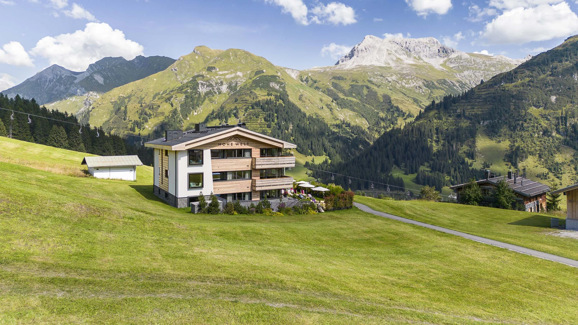 Modernes Berghaus auf grüner Alm mit Alpenbergen und blauem Himmel im Hintergrund
